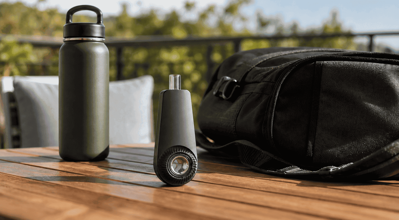 Portable dabbing device on an outdoor table beside a water bottle and everyday carry items